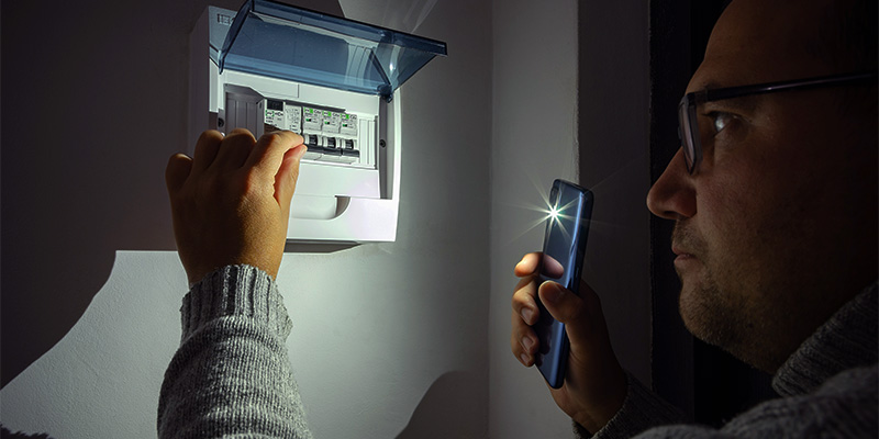 En man som lyser in i en elcentral med sin mobillampa.
