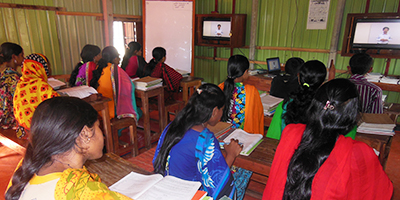 Flickor sitter i ett klassrum och kollar på en digital lektion.