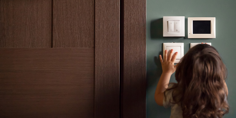 En liten flicka som står och pillar på strömbrytare på väggen.