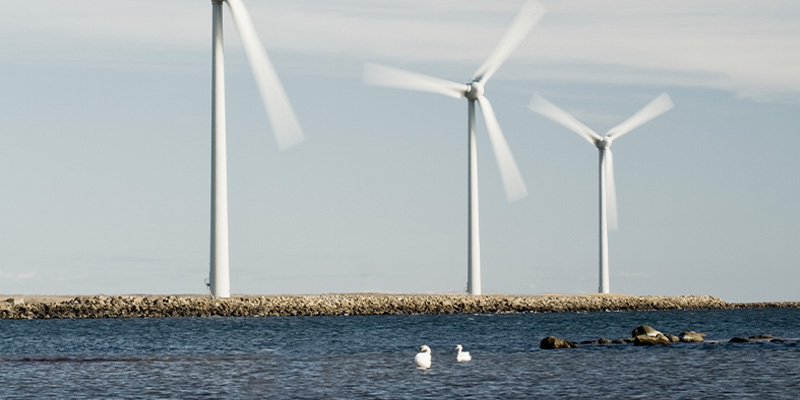 Tre vindkraftverk som snurrar på land framför vattnet.