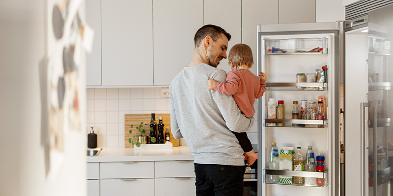 En pappa och ett barn står i ett kök framför ett öppet kylskåp.